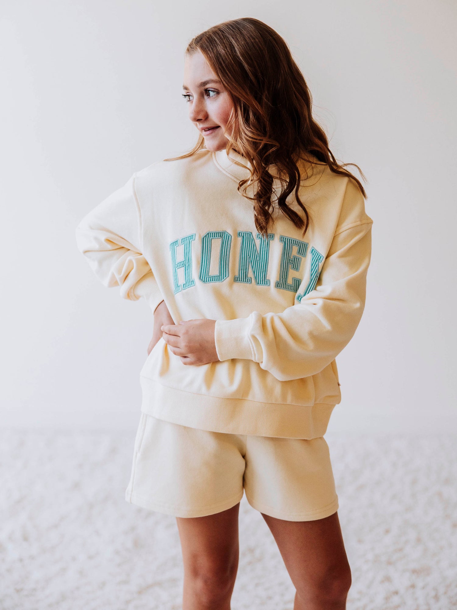 Model wearing a yellow, two-piece mock neck set. The top has HONEY on the front with blue pin stripes. Bottoms are the same color as the top. 