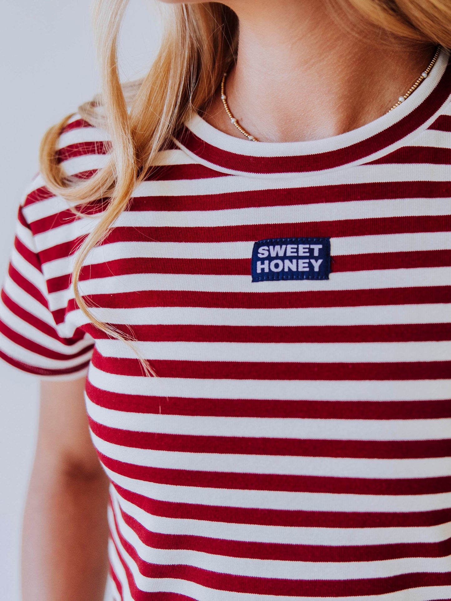 Close up of stitched sweethoney tag in the middle of crimson and ivory top. 
