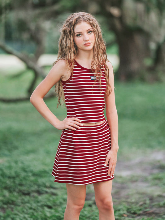Girl outside wearing a two piece skort set that is crimson and ivory striped. 