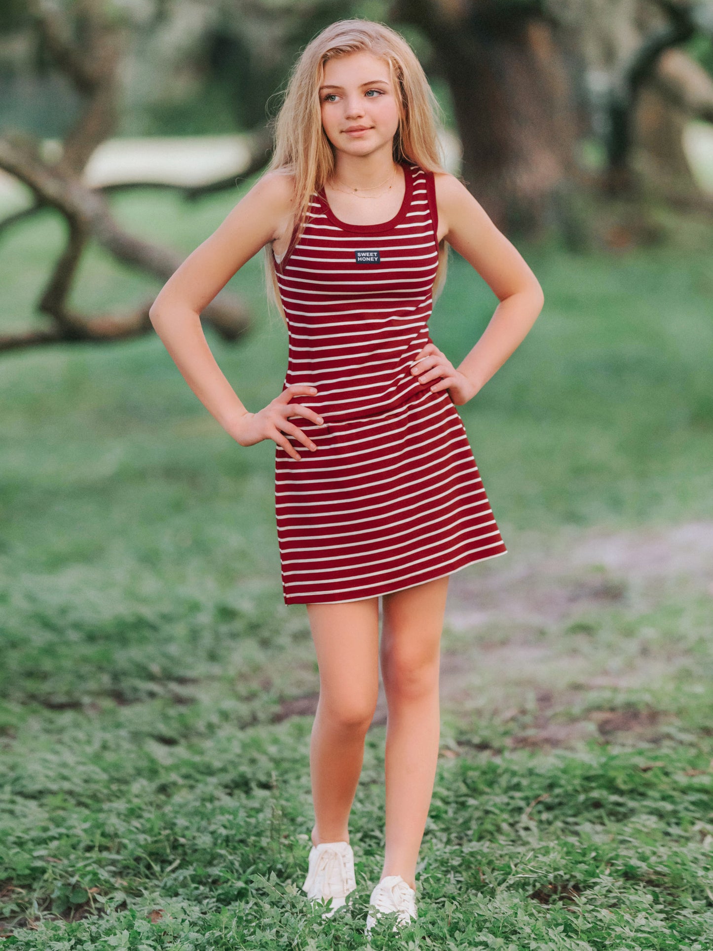 Girl outside wearing a two piece skort set that is crimson and ivory striped. Both of her hands are on her hips.