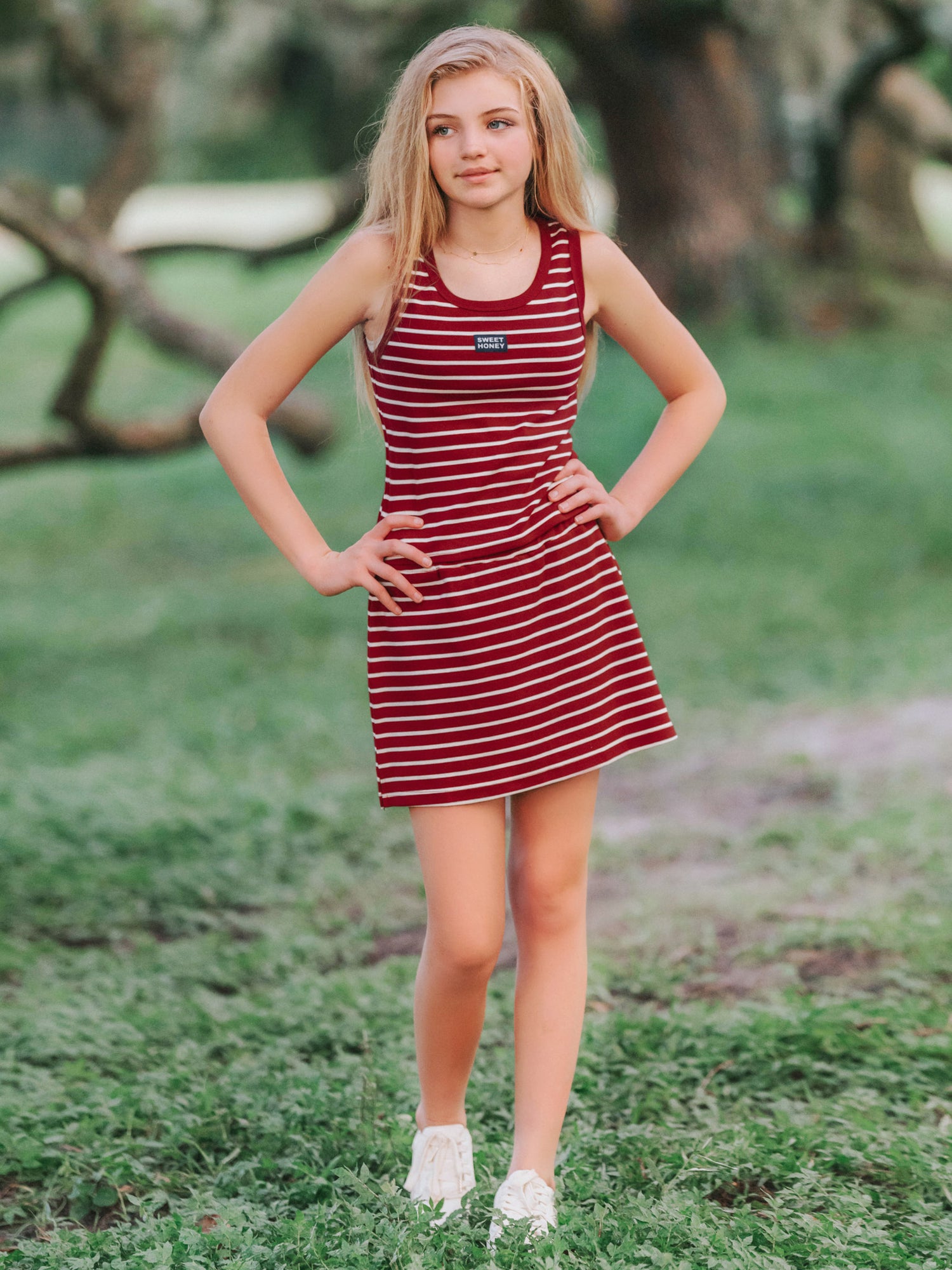 Girl outside wearing a two piece skort set that is crimson and ivory striped. Both of her hands are on her hips.