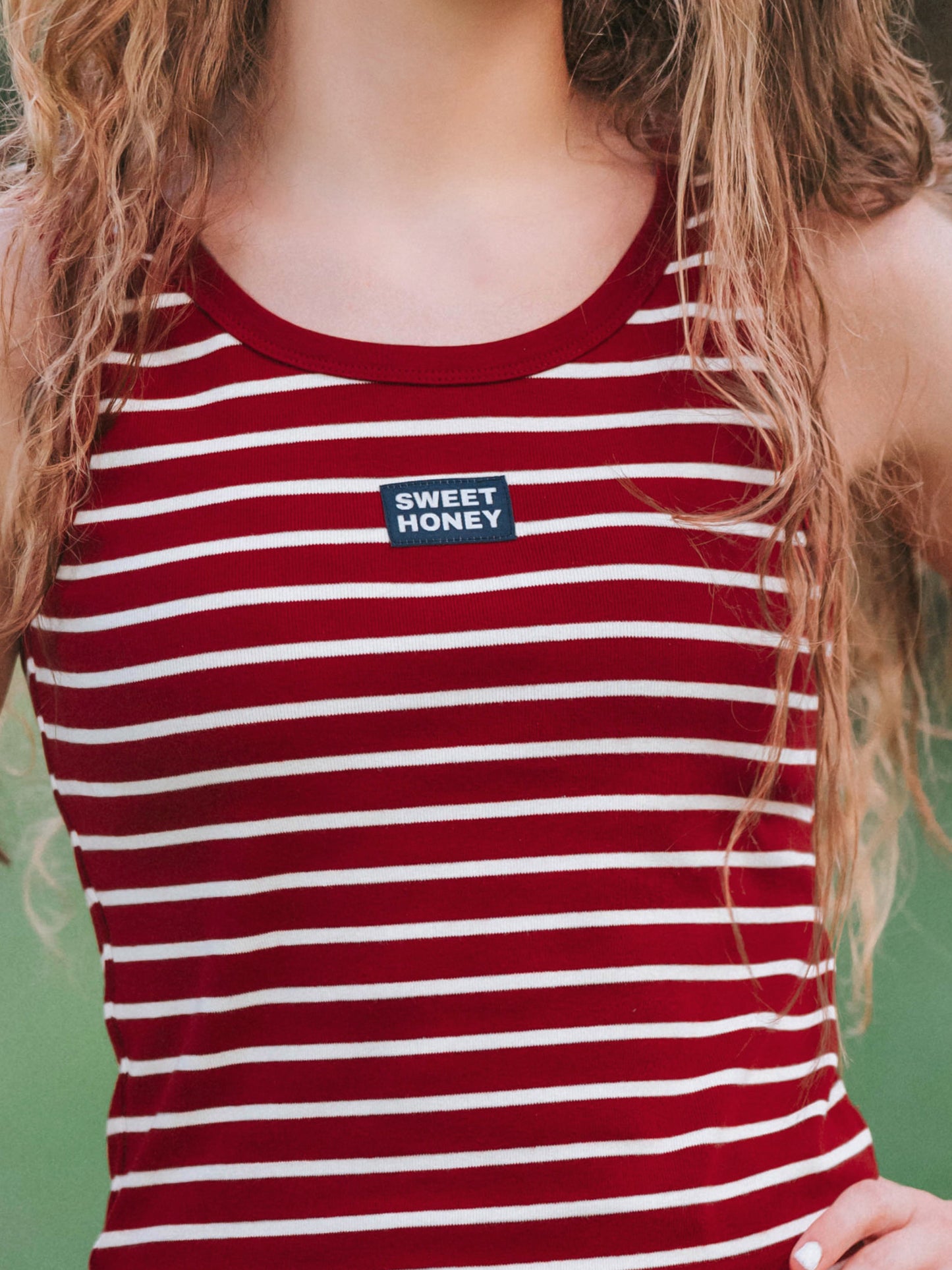 Up close shot of the Sweethoney logo centered on the chest of a crimson and ivory striped top