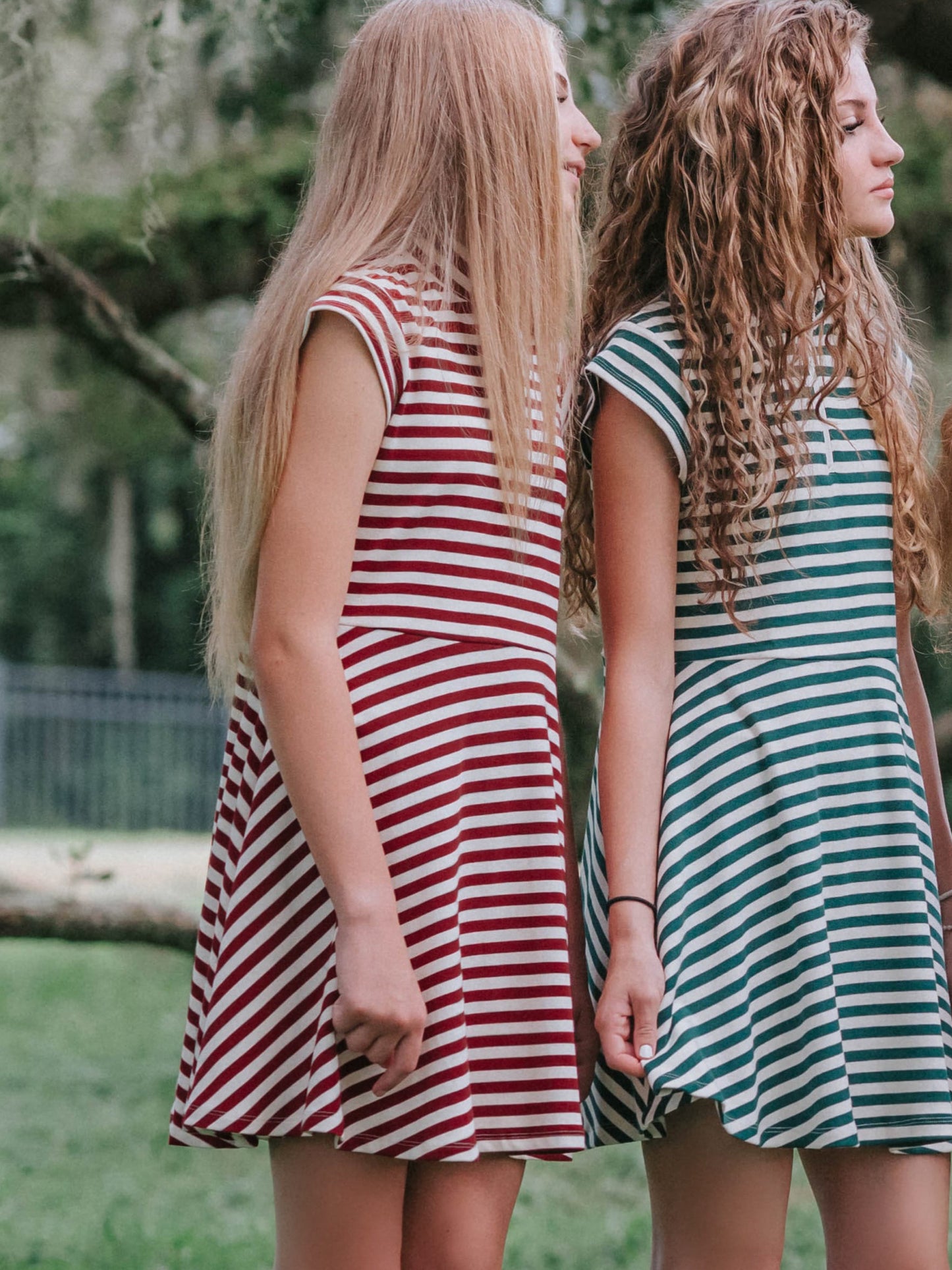 Two models outside wearing matching dresses in different colors. Left model's dress is crimson and ivory. Model on right is green and ivory. Both are looking away from camera.