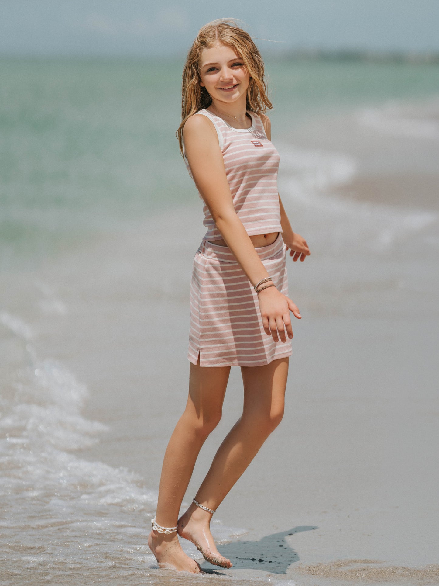 Model is outside on a beach wearing a two-piece matching pink and ivory striped skort set. Top is sleeveless. 