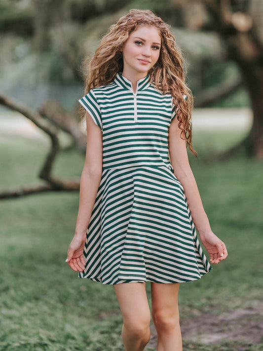 Girl outside in a greenery area smiling looking at the camera wearing a deep green and ivory striped dress.