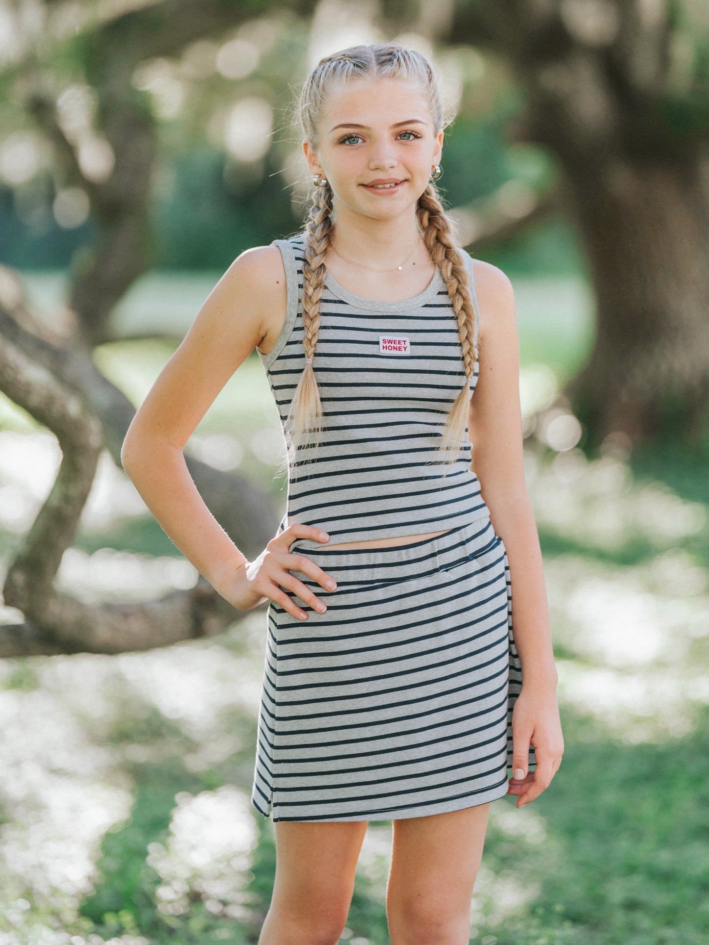 Model is outside in a green area wearing a two piece matching grey and navy striped skort set. She has one hand on her hip.