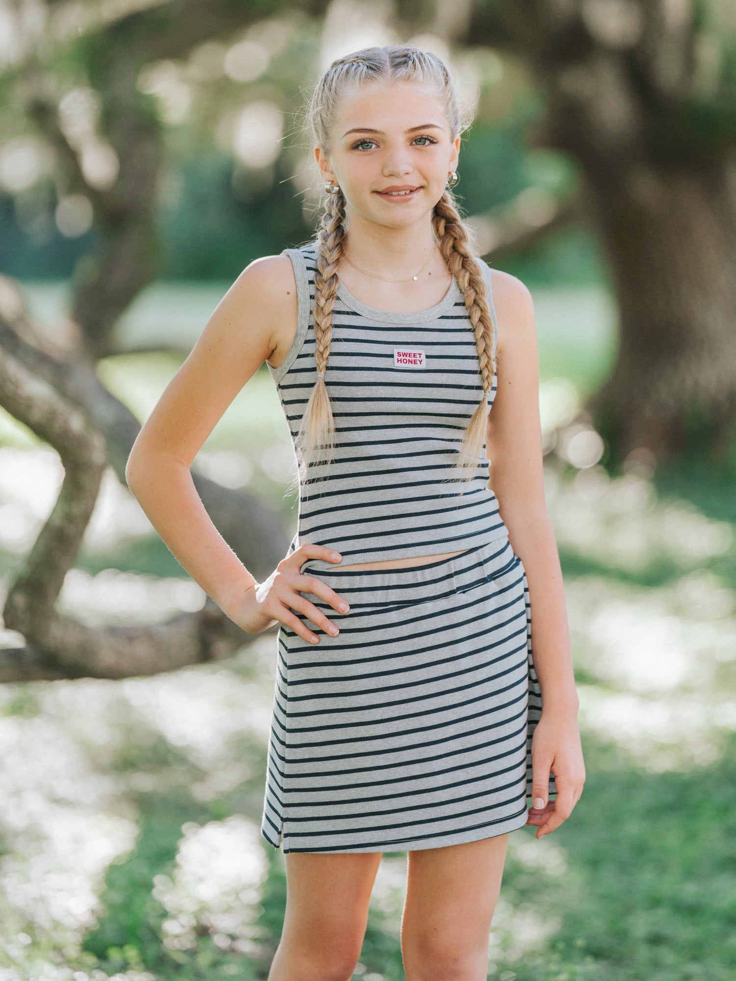 Model is outside in a green area wearing a two piece matching grey and navy striped skort set. She has one hand on her hip.