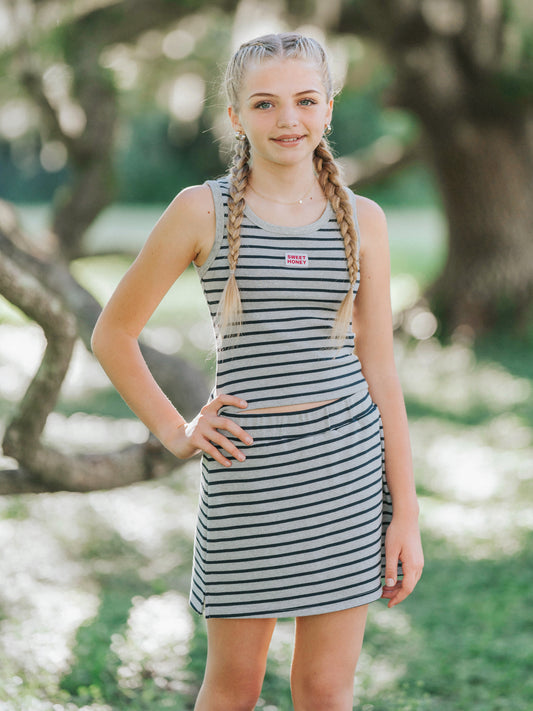 Model is outside in a green area wearing a two piece matching grey and navy striped skort set. She has one hand on her hip.