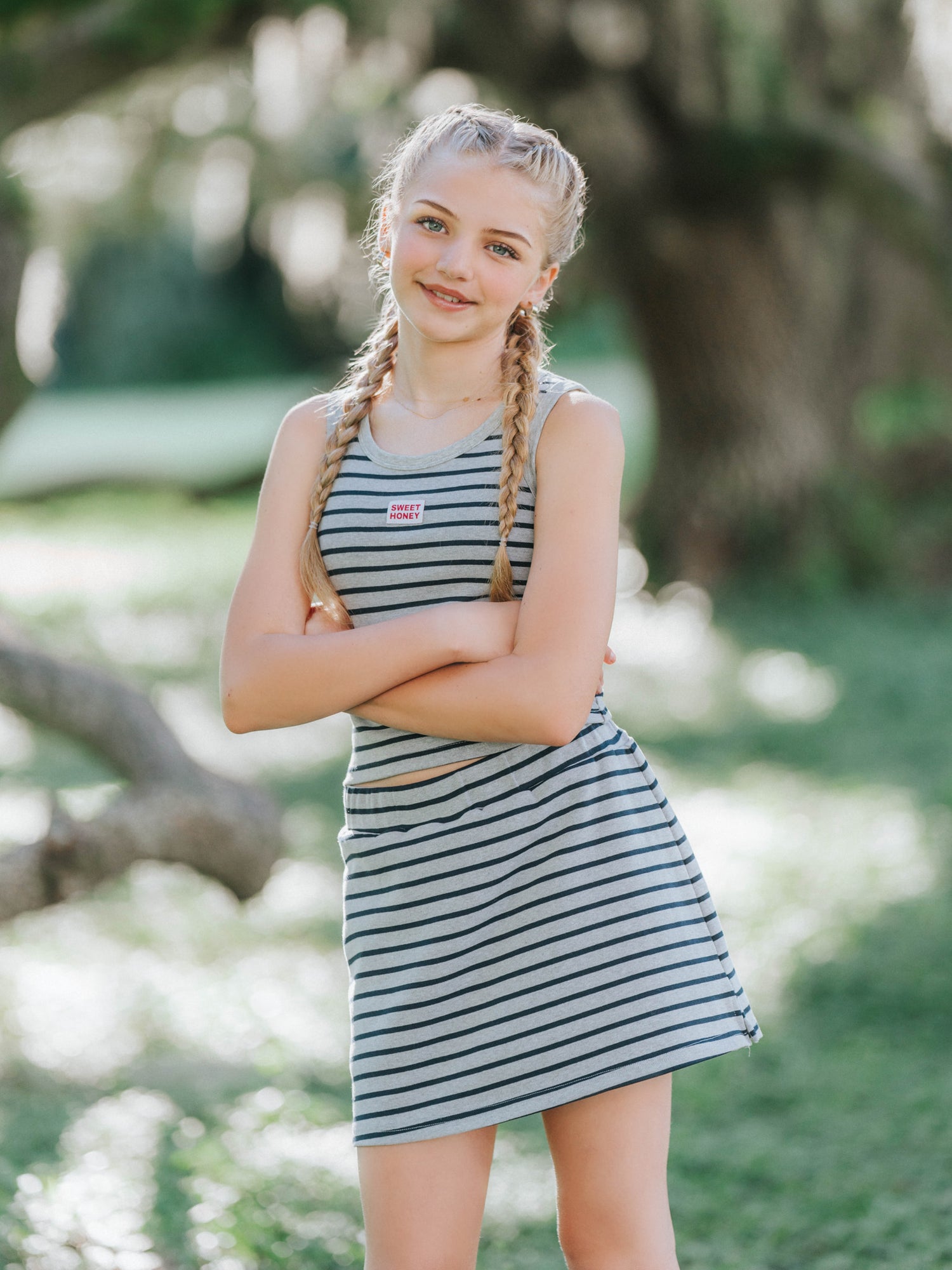 Model is outside wearing a navy and grey striped skort set with her arms folded. 