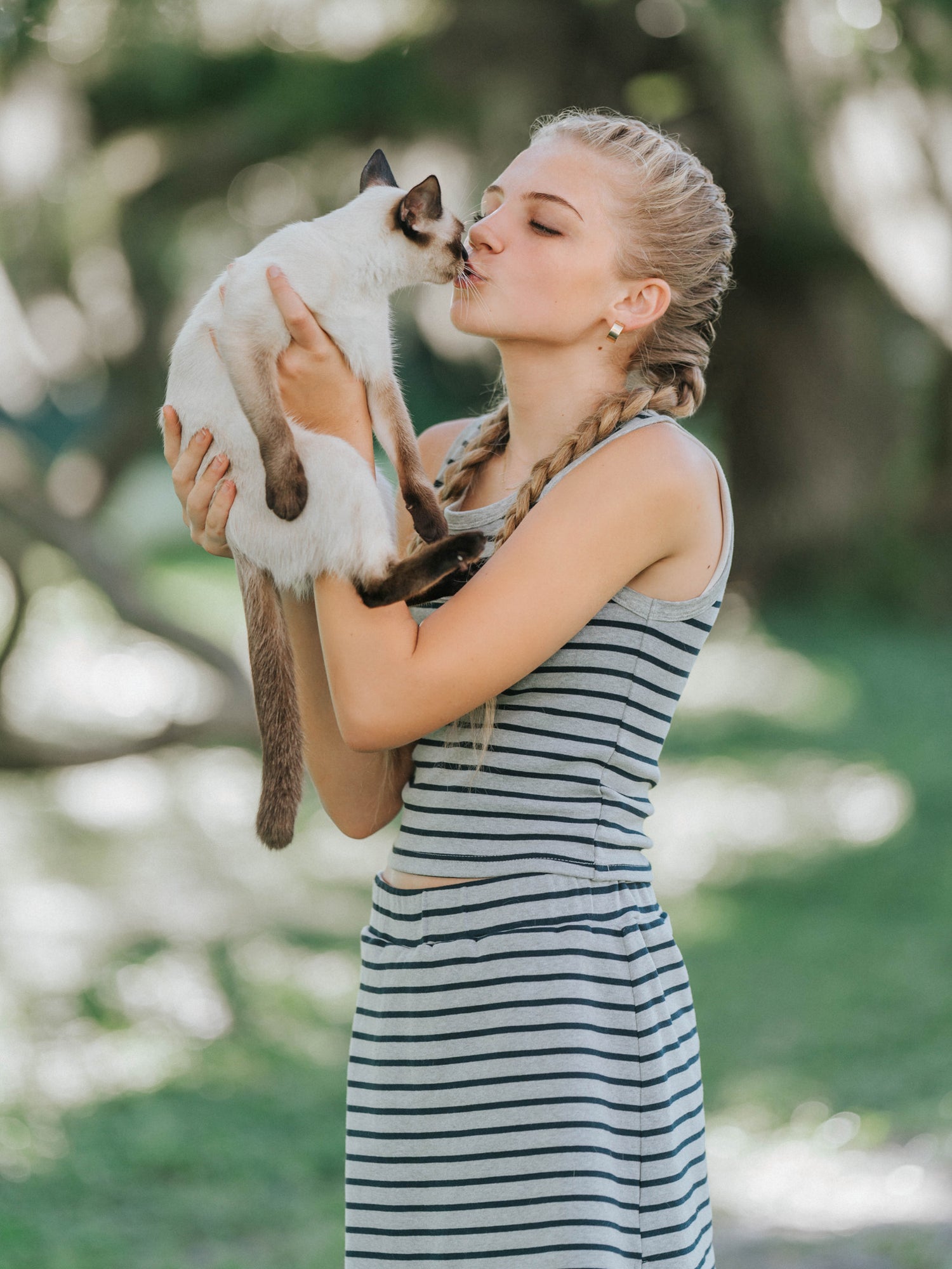 Model is outside and is holding a Persian cat giving it a kiss. Model is wearaing a two piece matching skort set that is grey and navy striped. 