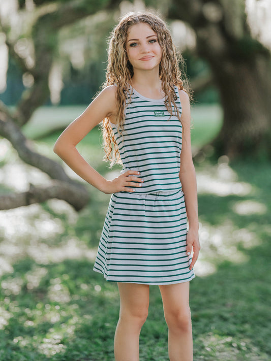Model is outside and has her hand on her hip. Model is wearing a two-piece skort set that is greyish and green striped. Shirt is sleeveless. 