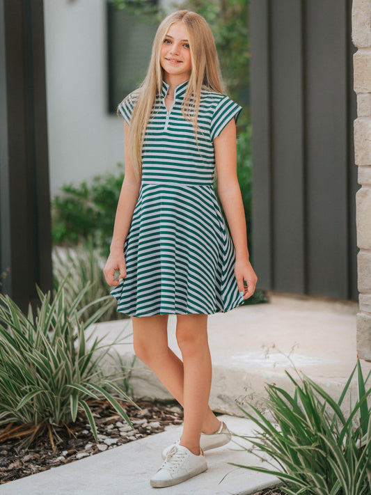 Model is outside on porch wearing a lavender and green stiped dress with white canvas shoes. 