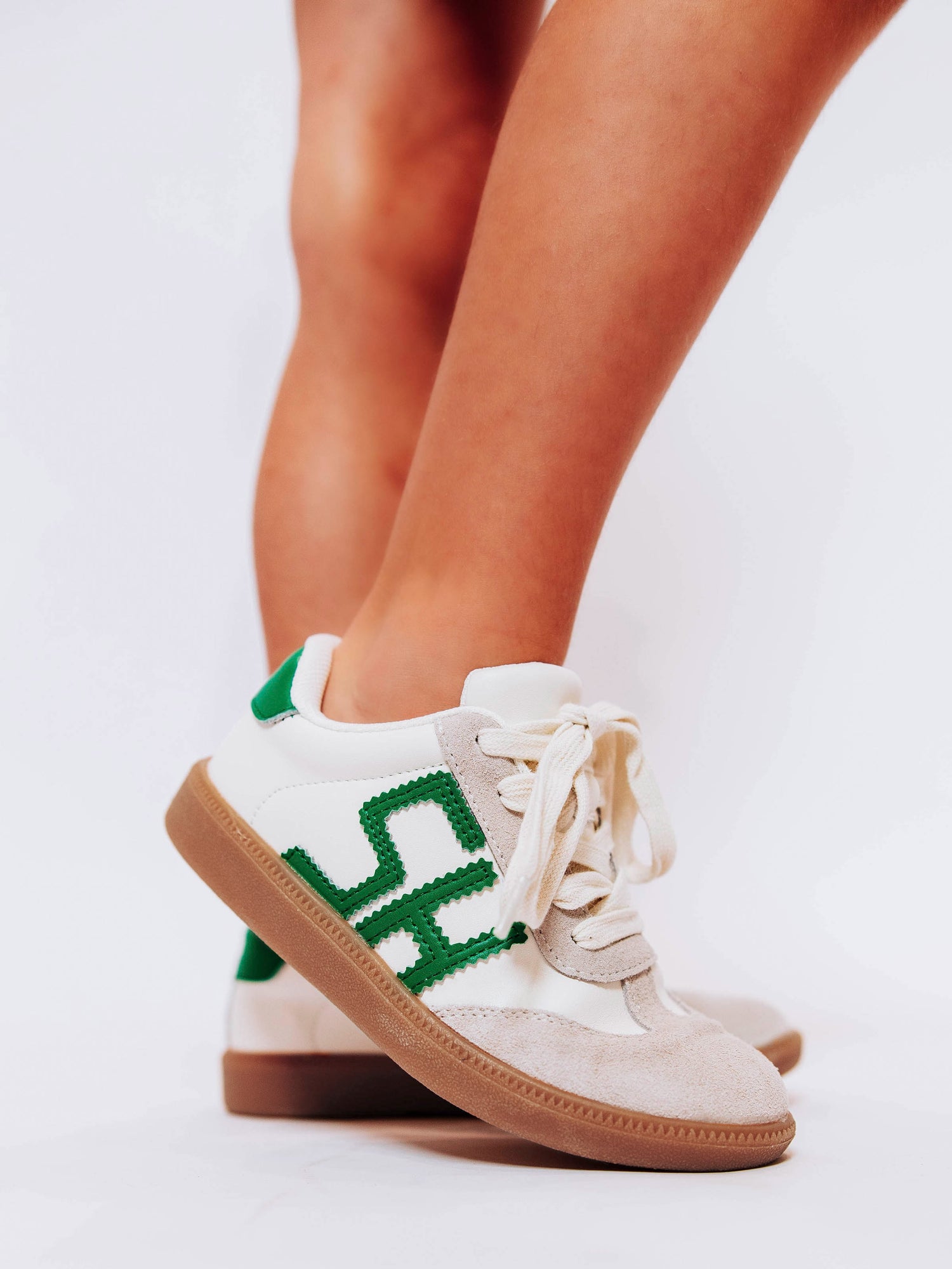 Close shot of girl wearing white sneakers with "SH" lettering stitched in green leather on outer side of shoes along with green heel caps.