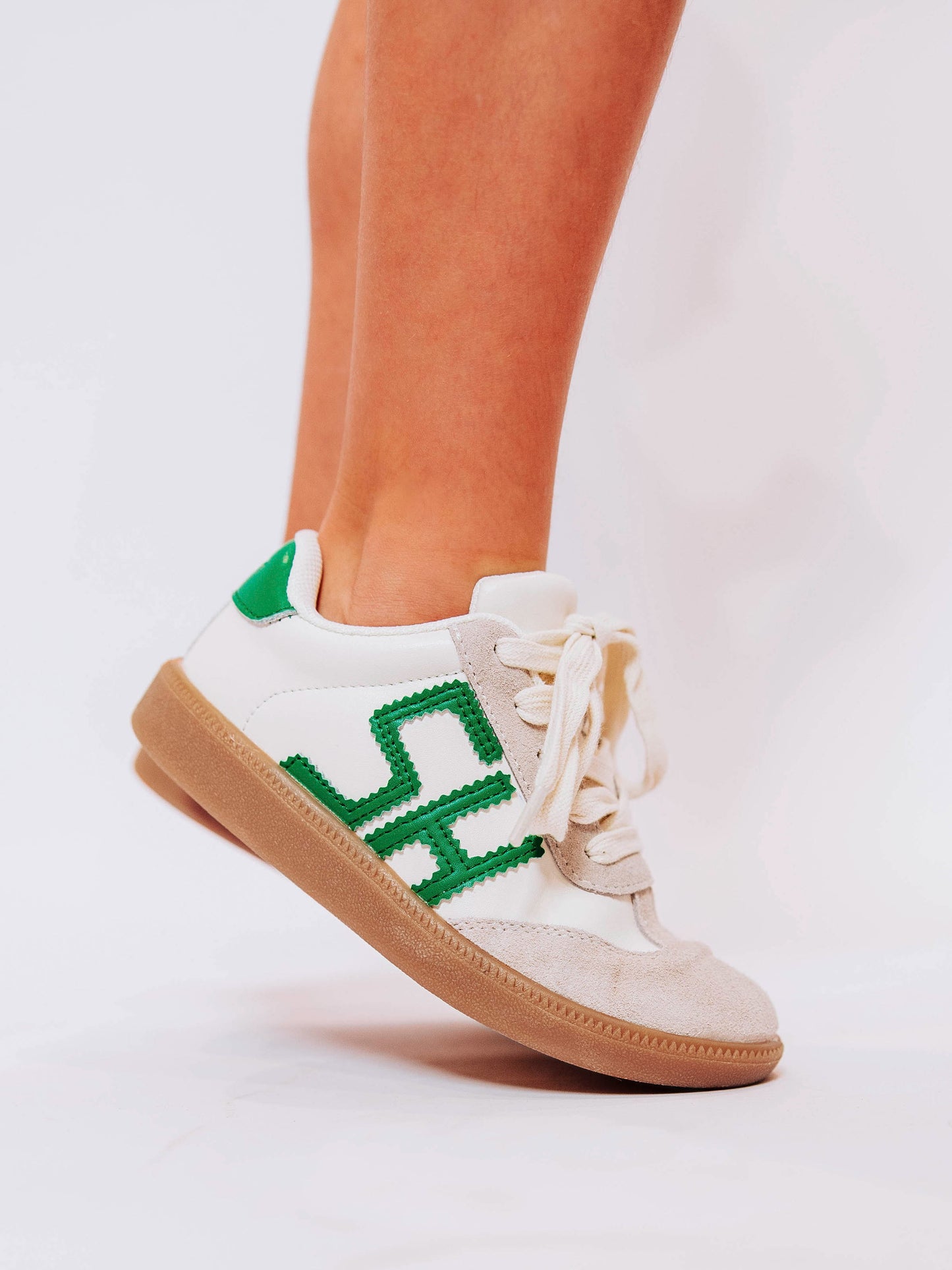 Close shot of girl wearing white sneakers with "SH" lettering stitched in green leather to outer side of shoes and green heel caps.