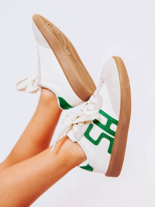 Close shot of girl wearing white sneakers with stitched green leather "SH" letters on outer side and green heel cap.