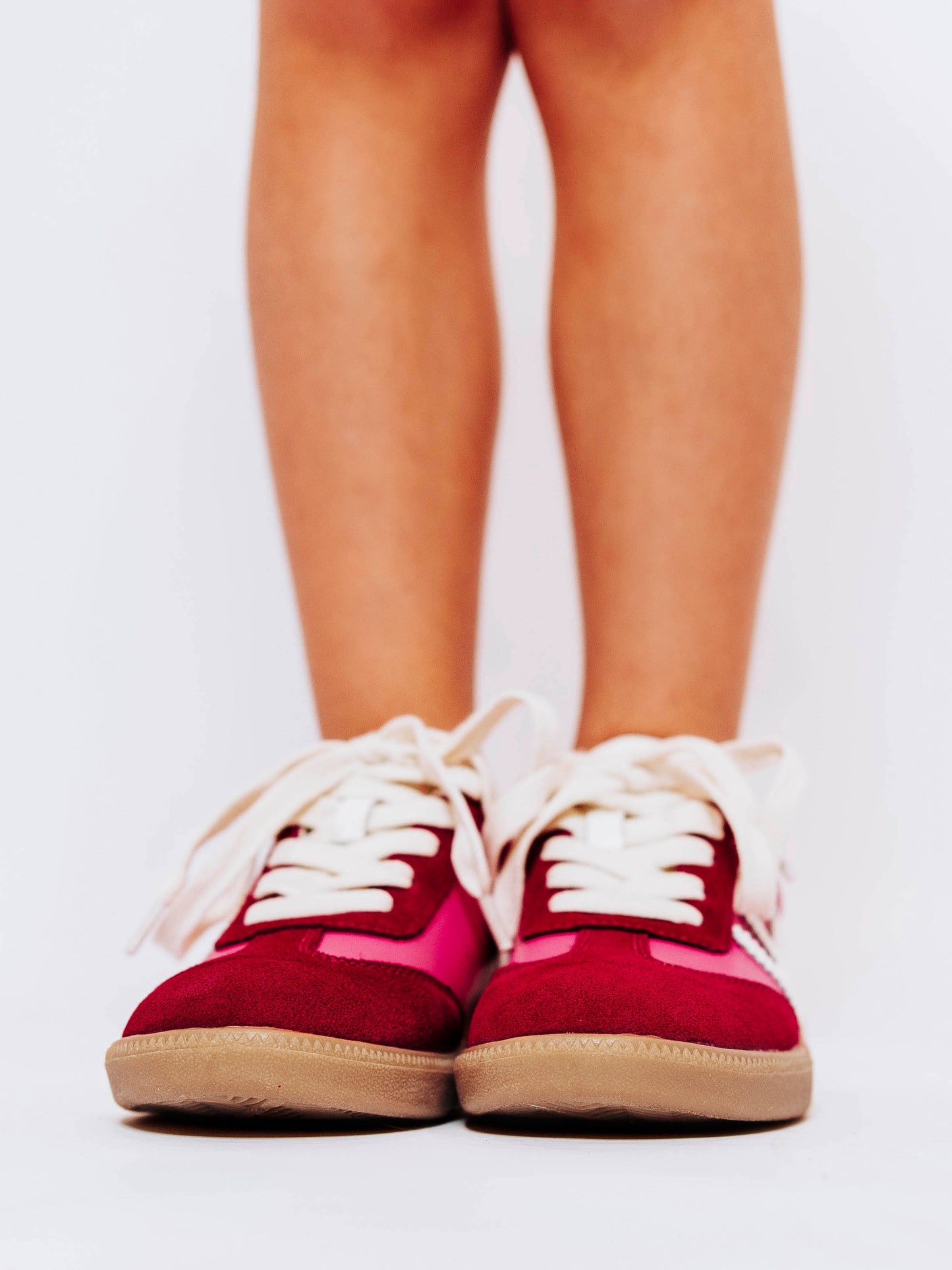 Close shot of front side of girl wearing pink sneakers with red suede secondary details and white laces.