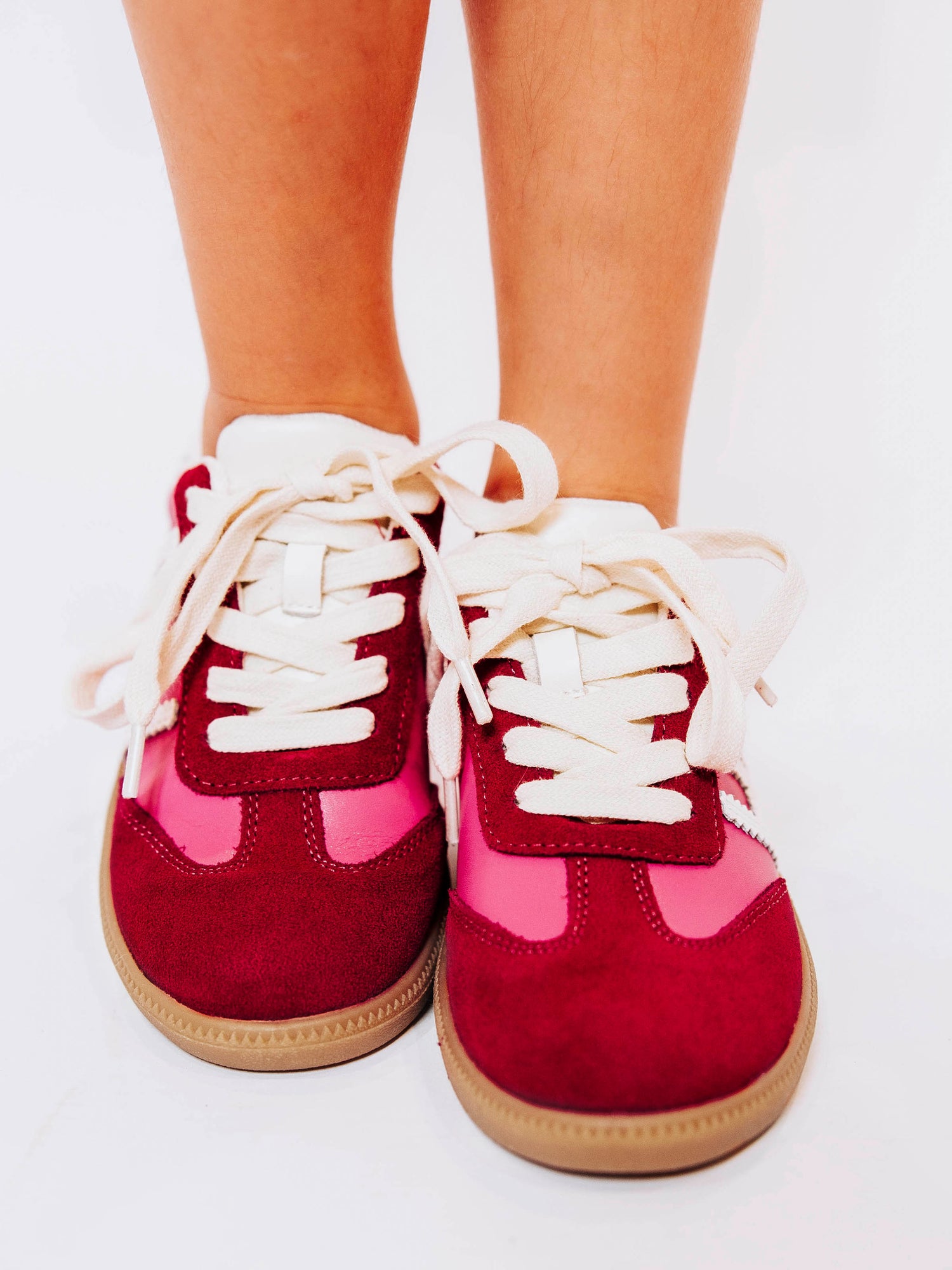 Close shot of girl wearing pink sneakers with red suede secondary details and white laces.