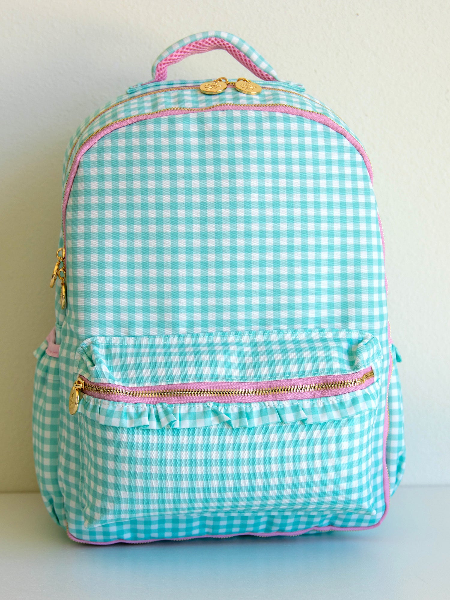 Mint green gingham backpack with pink zipper accents and gold zipper pulls.
