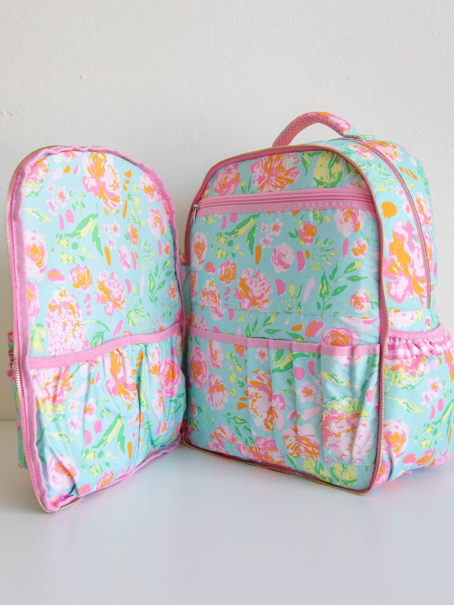 Shown a floral and colorful backpack with the front zippered pocket opened. You see the different storage compartments. 