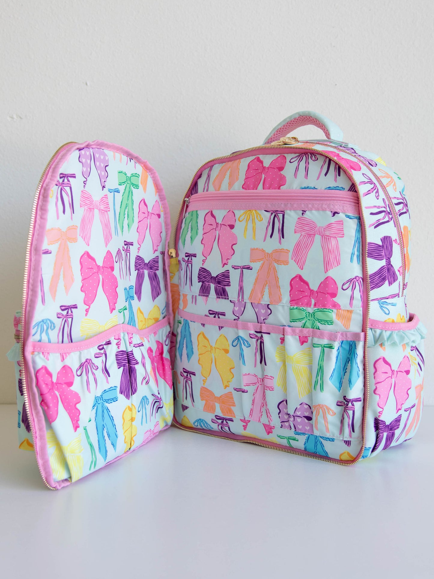 Vibrant bows printed backpack with front zipper compartment open with different compartments shown for storage