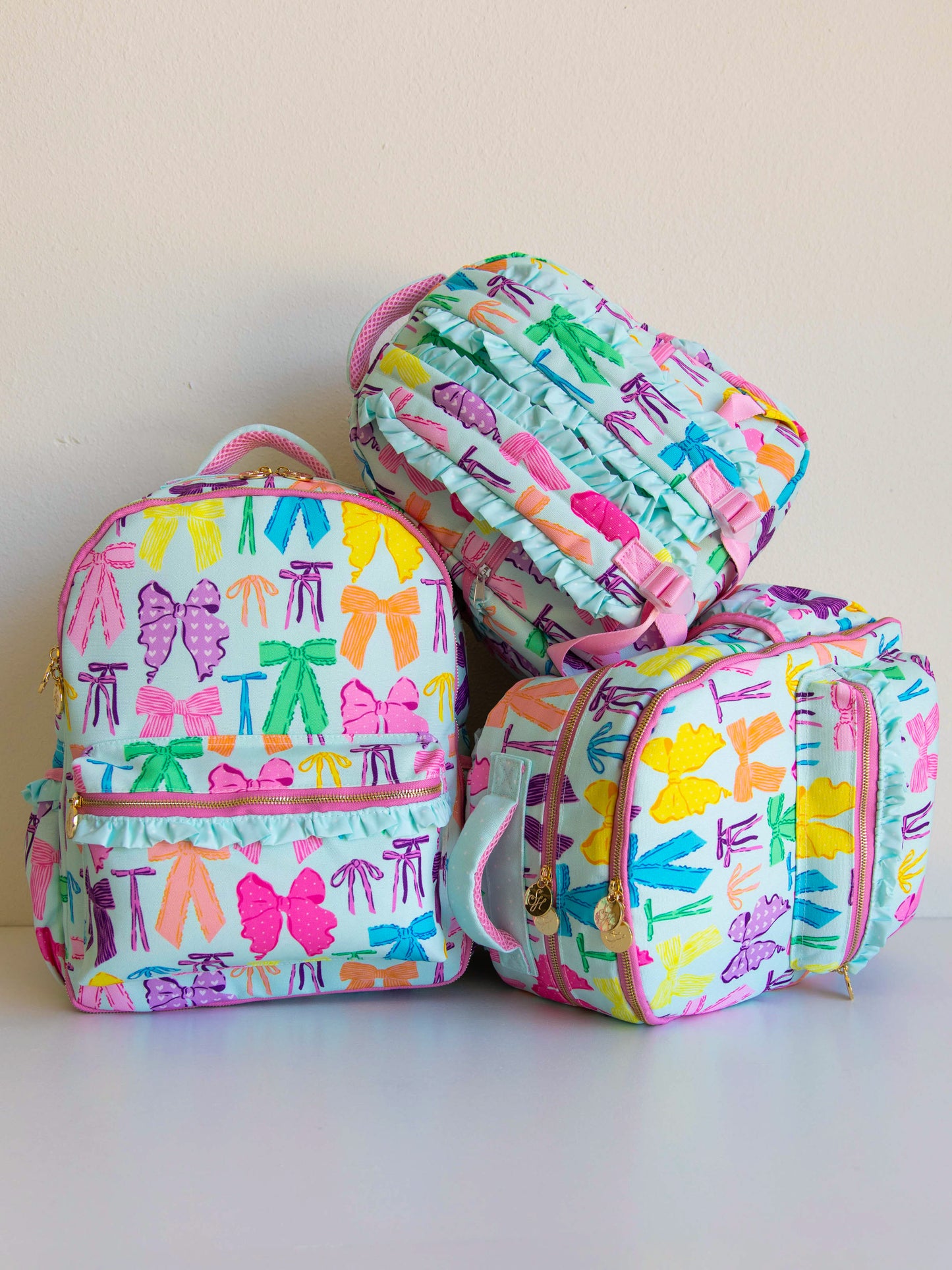 Three different sized backpacks stacked that have vibrant colored bows