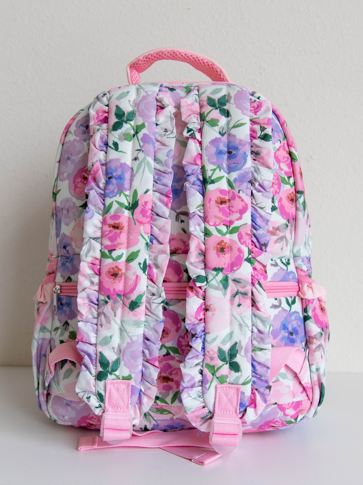  colorful floral backpack with a purple gingham bow attached to the backpack. gold zippers and zipper pulls. back strap ruffles