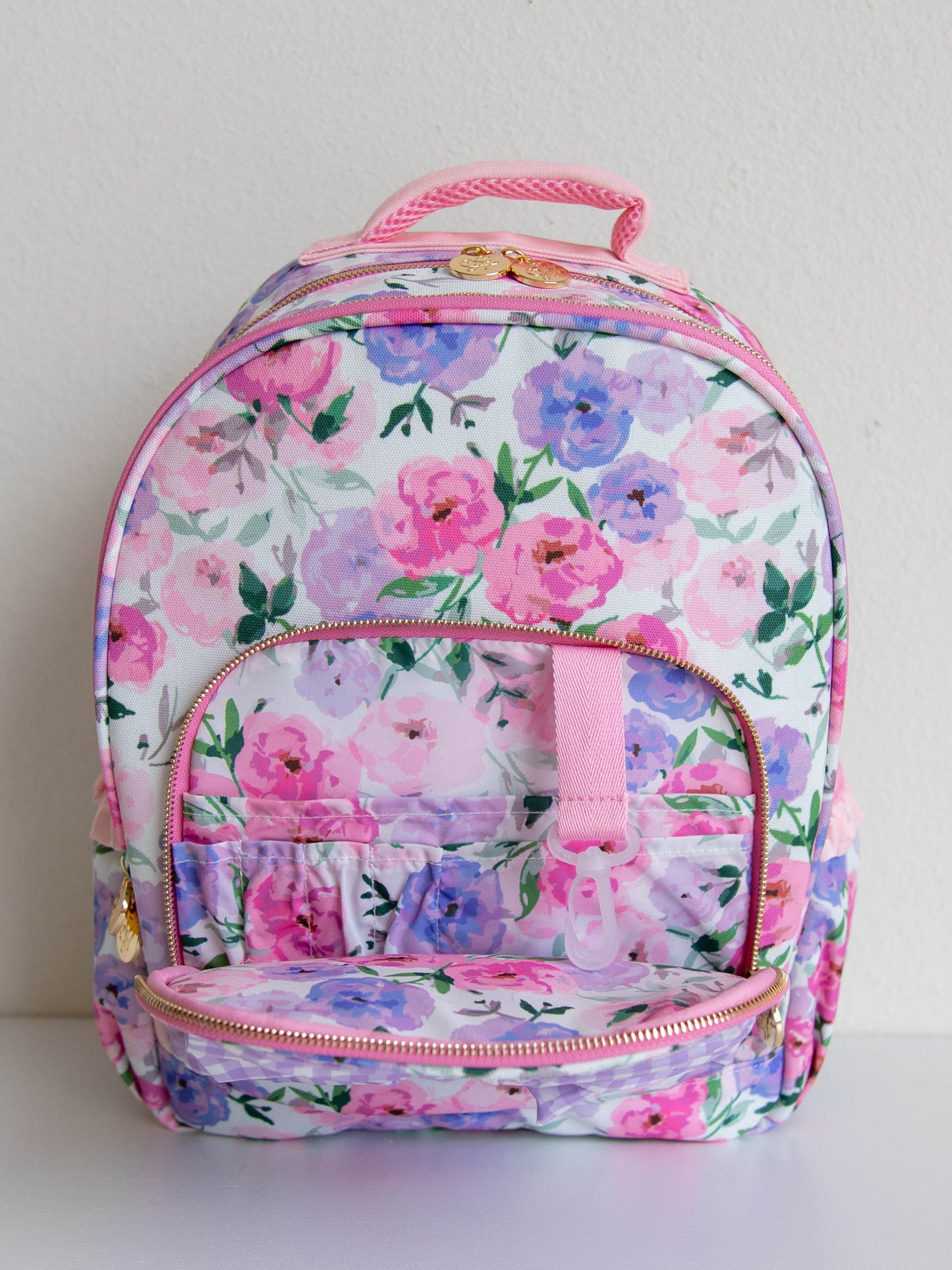  colorful floral backpack with a purple gingham bow attached to the backpack. gold zippers and zipper pulls. front zipper open to show different compartments