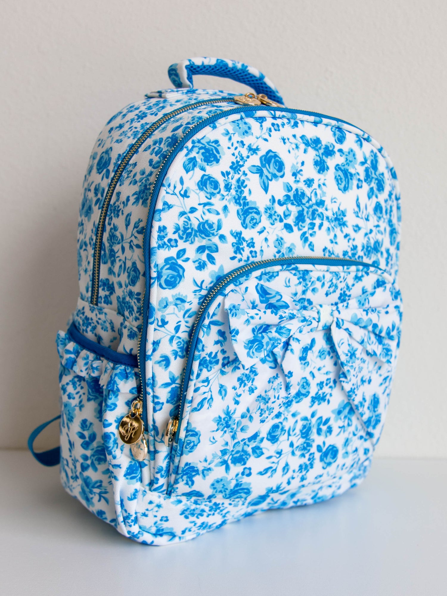 Blue floral backpack with gold zippers and an attached bow on the front