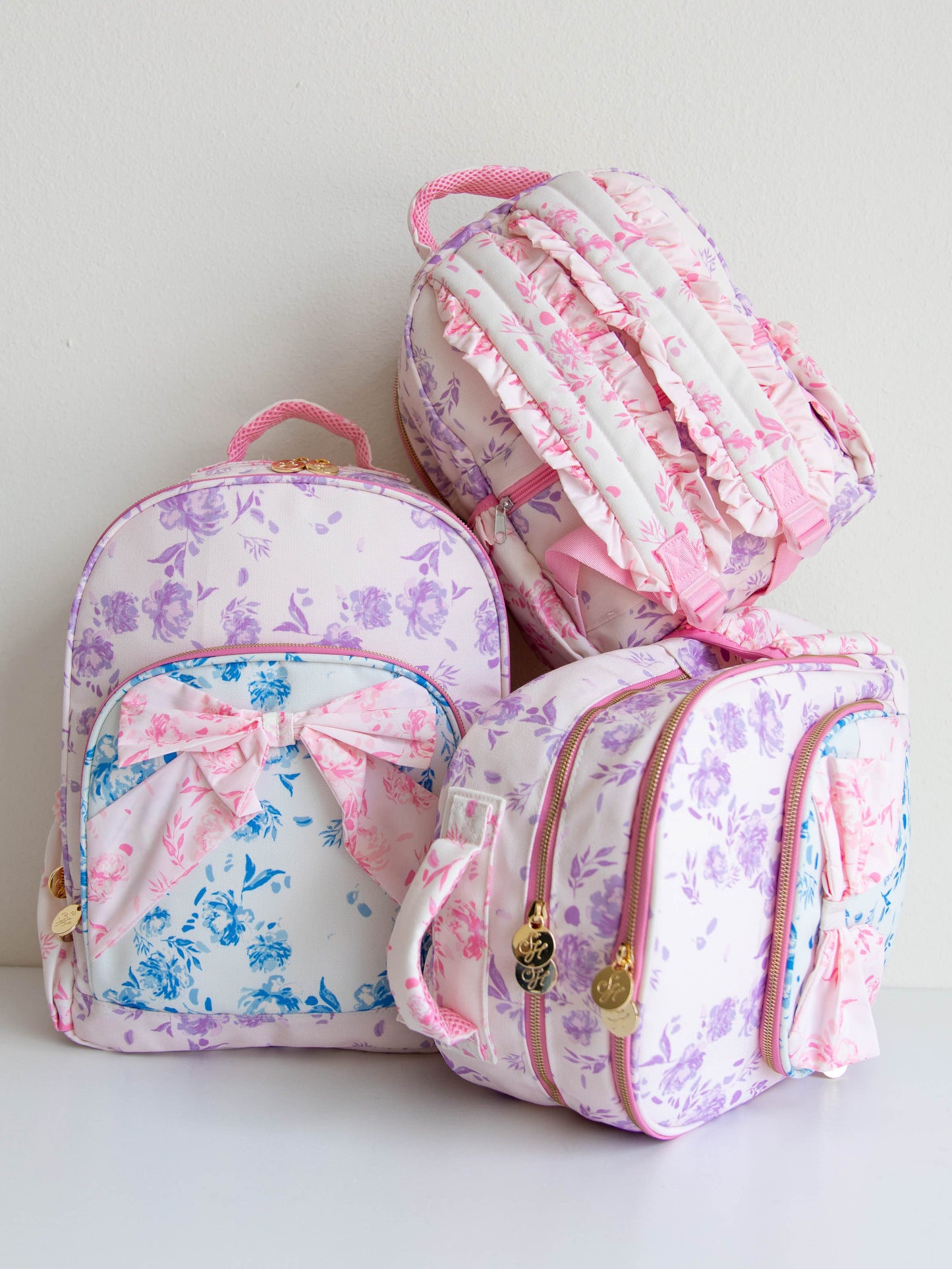 Three different size backpacks that all have the same colorful, floral, and attached bow. 