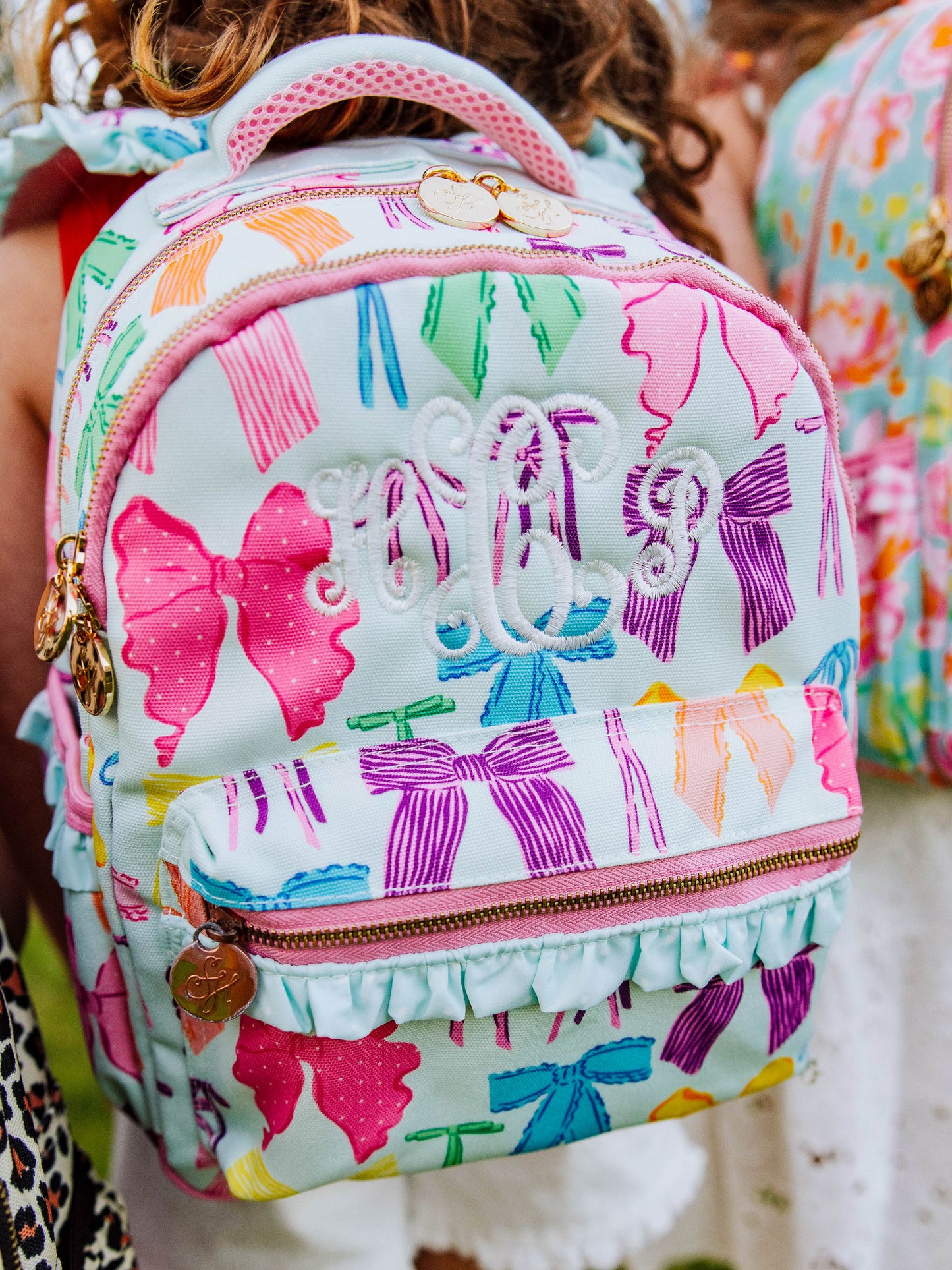 Girl wearing a Vibrant bows printed backpack with customized embroidery, gold zippers and zipper pulls, and a handle