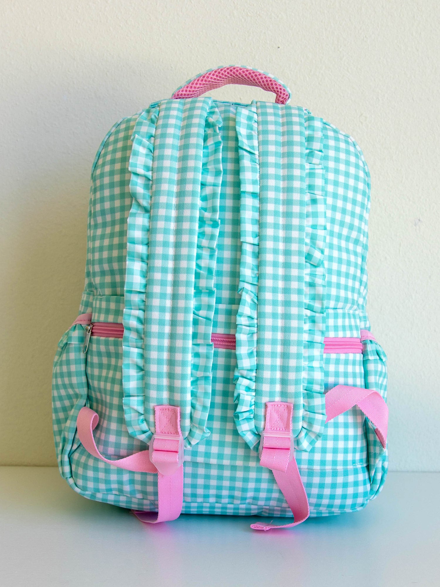 back of mint green gingham backpack that shows ruffled straps. Pink accents. 