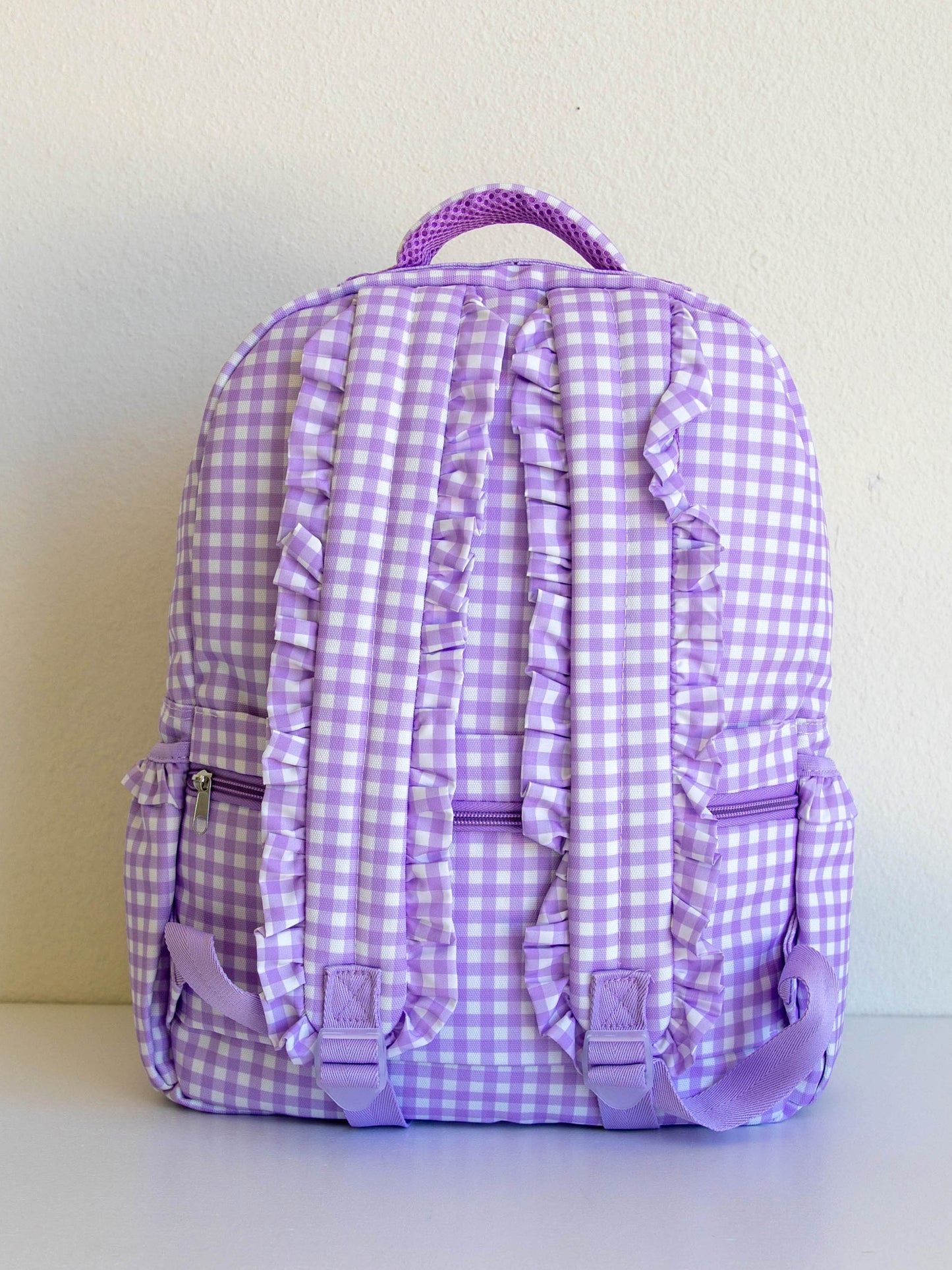 backside of purple gingham backpack. straps have ruffles. 