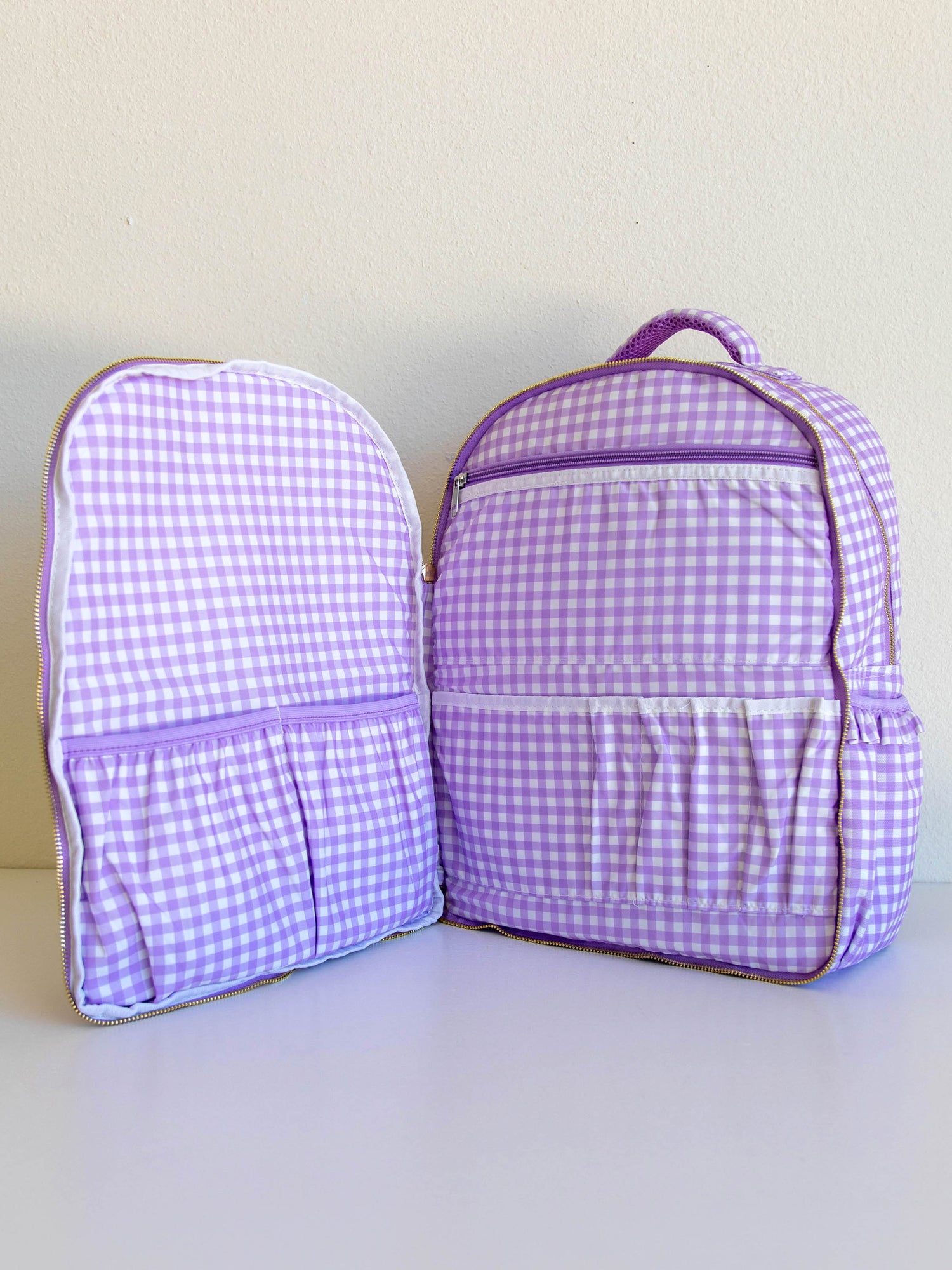 Single purple gingham backpack opened up to see different storage compartments. 