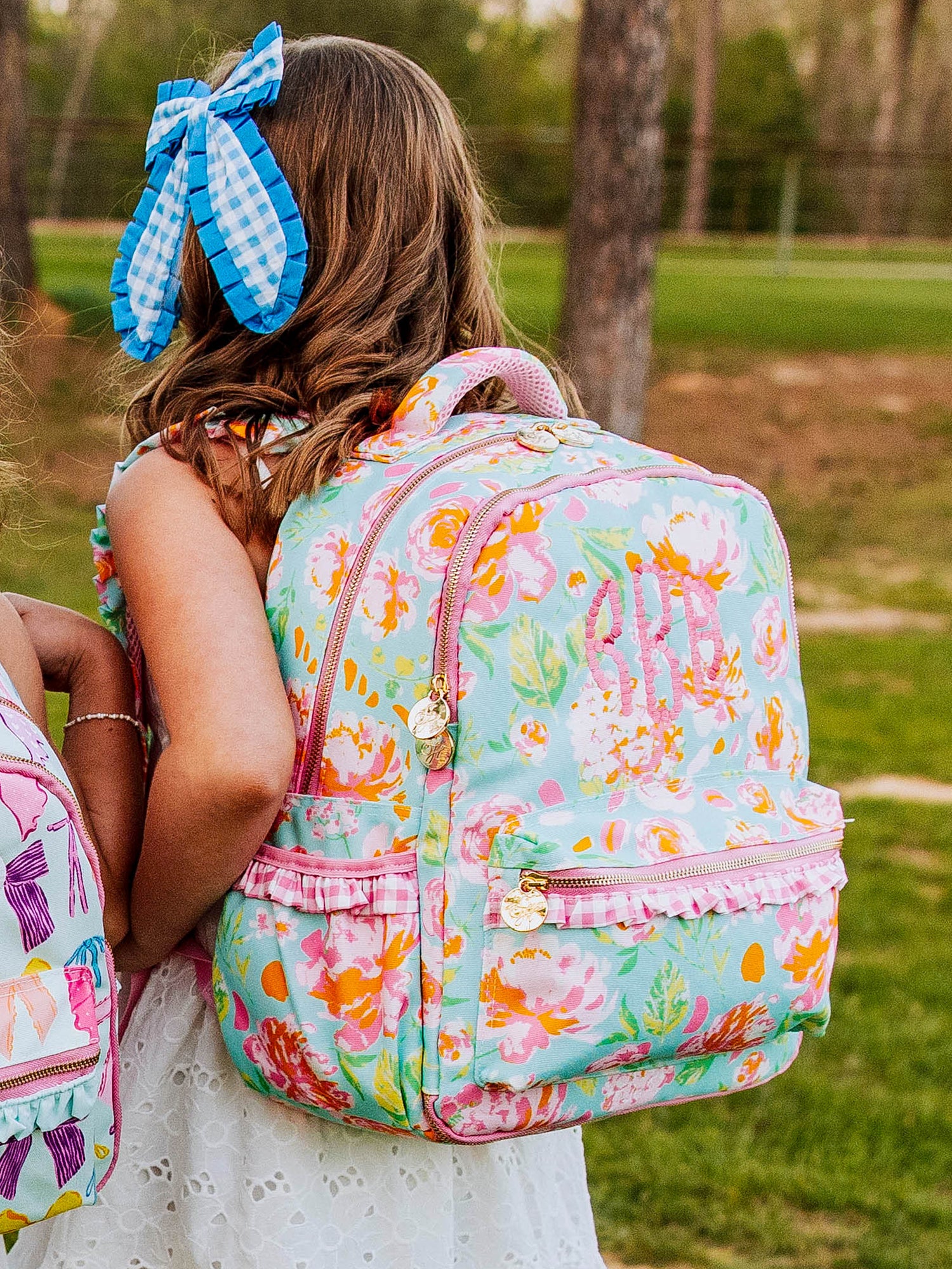 Girl wearing a colorful, floral backpack that has beaded embroidery on it