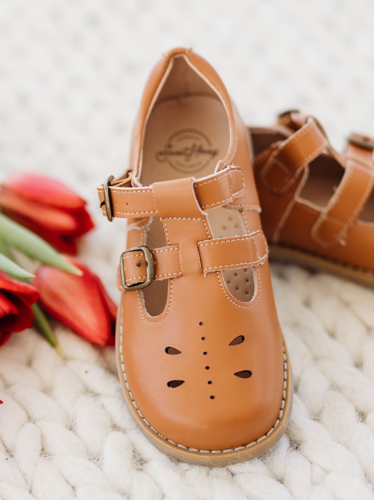 A pair of camel colored genuine leather rubber soled shoes with two adjustable metal buckles and ventilation holes across the toe area in a dragonfly type pattern. 