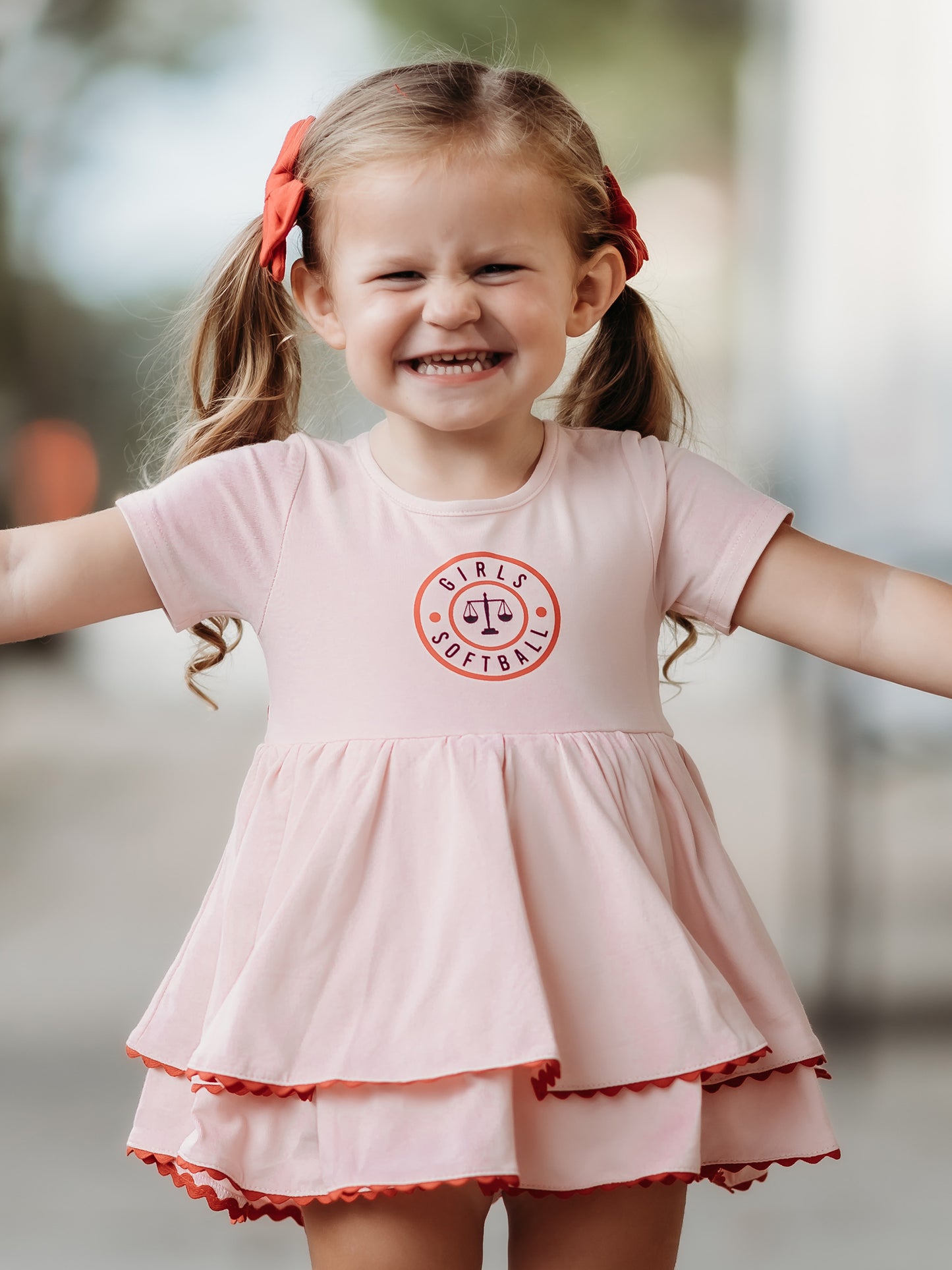 This image of a girl features the product Belle Bubble - Girls Softball. This pink double skirted dress has the same Girls Softball logo on the front as our Girl’s Softball Dress & Hat.