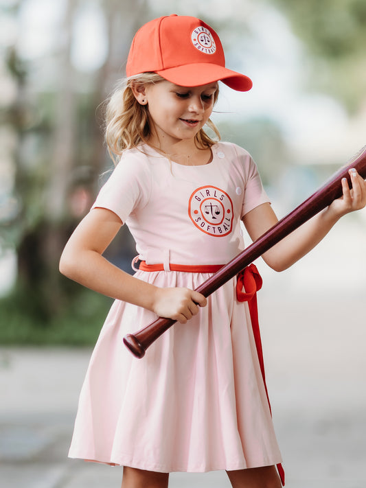 This image of a girl features the product Softball Dress - Girls Softball. This pink short sleeve dress has the same Girls Softball logo on the front as our Girl’s Softball Bubble & Hat.