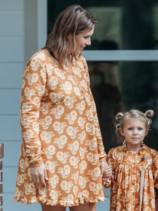 Women's Gown - Autumn Sunflowers. This long-sleeved gown comes in a pattern of tan sunflowers on a burnt orange background.