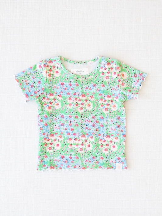 Frilled Sleeve Shirt - Wildflowers. It comes in a pattern of light blue and pink flowers on a green background.