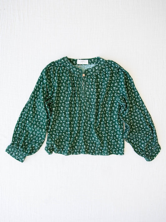 Women's Long Sleeve Blouse - Dark Green Floral. This billowy long sleeve top has a keyhole neck with a single button. It comes in a pattern of small cream flowers on a dark green background.