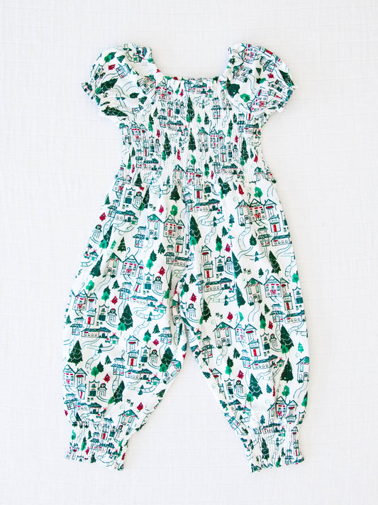 Smocked Romper - Christmas Town. This short sleeved smocked romper comes in a pattern of Christmas themed buildings and evergreens on a snowy background.