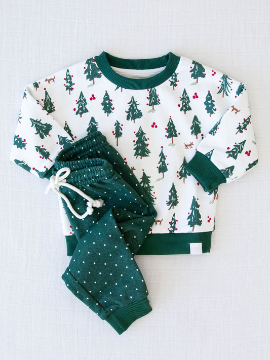 Sweatshirt Set - O Christmas Tree. The top is a pattern of evergreen trees with red ornaments on a snowy background. The bottoms come in a pattern of white polka dots on a deep green background.