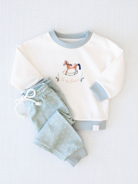 Sweatshirt Set - O Christmas Tree. The light blue top features an illustration of an old rocking horse and the words ‘Tis the Seaon’ in light pink. The bottoms are a pattern of white polka dots on a dusty light blue.