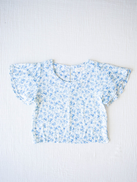 Classic Flutter Top - Blue Jay Floral. This top has a keyhole back and flowy double ruffle sleeves. It is a blue rose pattern on a pale background.