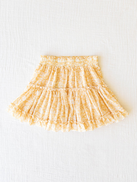 Classic Tiered Mini Skirt – I’ve Got Sunshine. This double layered short skirt features a smocked waistband as well as ruffled seams and hem. It is a pattern of white flowers on a bright yellow background.