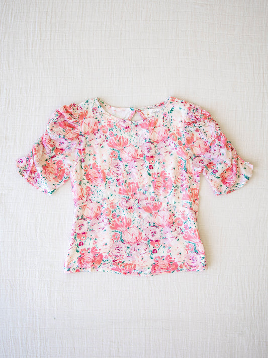 Classic Smocked Cutout Top – Starburst Pink. This short sleeve top has a smocked and keyhole back, and synched sleeves. It is a vibrant pattern of large bursting pink blooms and small green leaves.