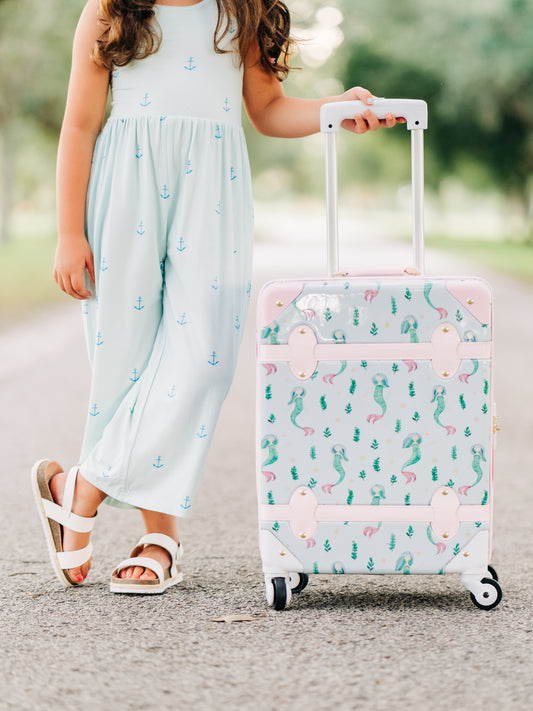 This image of a girl features the product Lennon Traveling Luggage – Sea Princess. The outside of this luggage is a pattern of mermaids and little green sea plants on a pale blue background. The inside lining is a pattern of pale blue starfish like stars on a blue background.