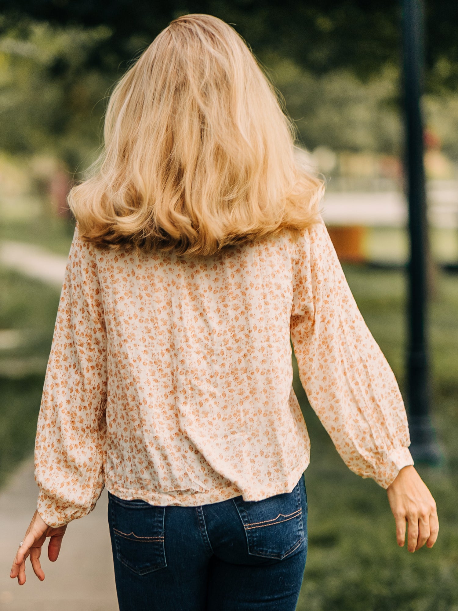 This image of a woman features the product Women's Long Sleeve Blouse - Golden Floral. This billowy long sleeve top has a keyhole neck with a single button. It comes in a pattern of small gold roses on a cream background.