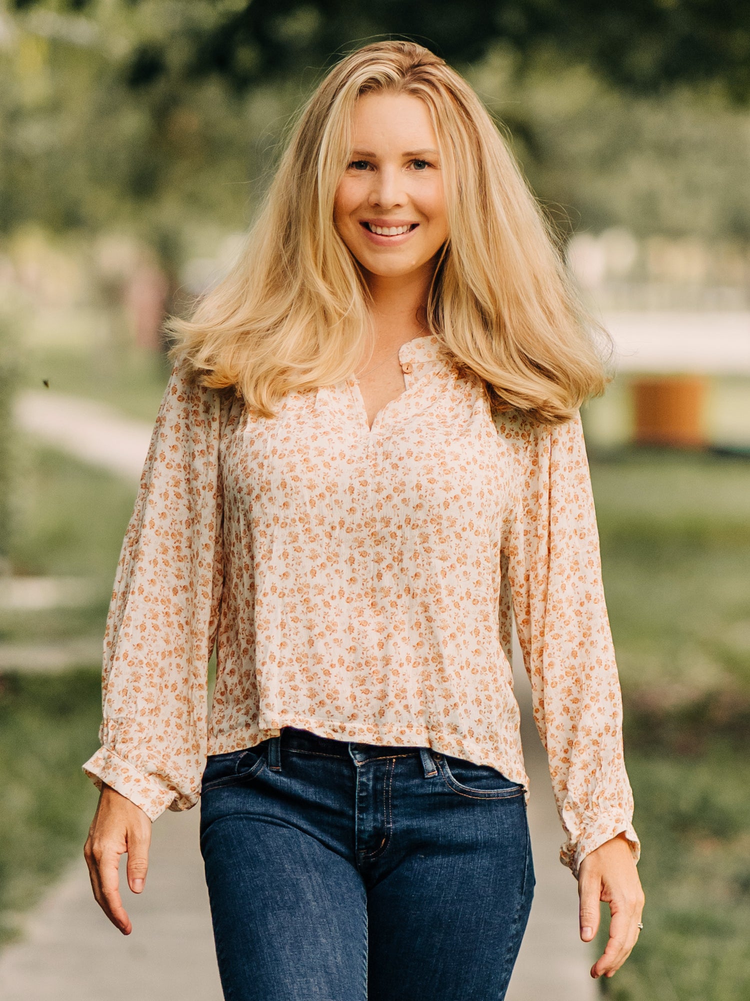 This image of a woman features the product Women's Long Sleeve Blouse - Golden Floral. This billowy long sleeve top has a keyhole neck with a single button. It comes in a pattern of small gold roses on a cream background.