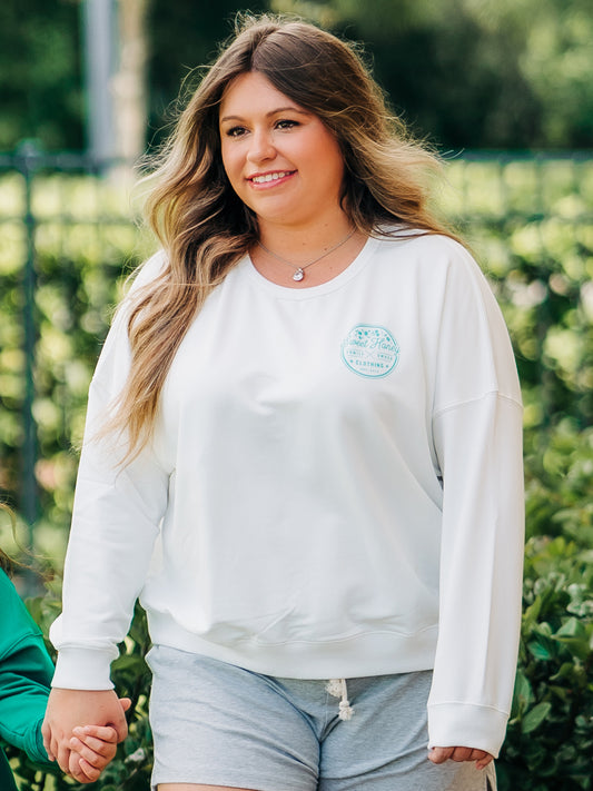 This woman is wearing Women's Sporty Crewneck – Ivory. This Sporty Crewneck comes in an almost white color with a with the SweetHoney logo in turquoise.